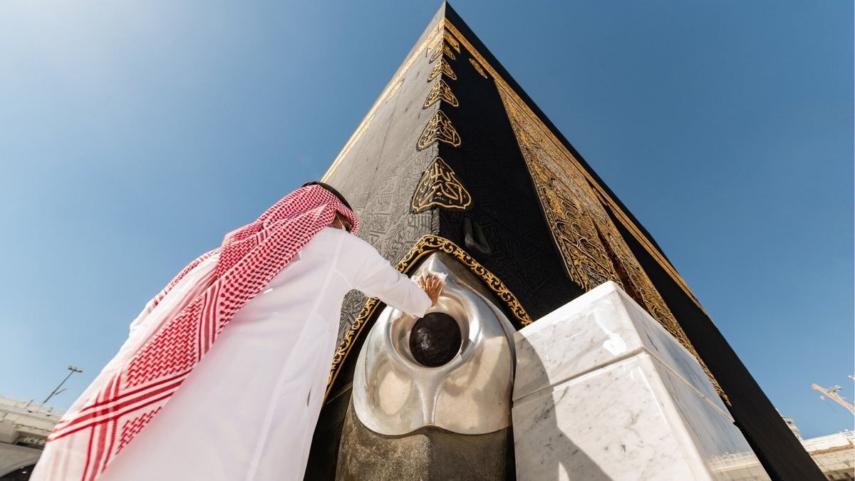 The corner of the Kaaba with the Black Stone set in its silver frame, and a man reaching toward it