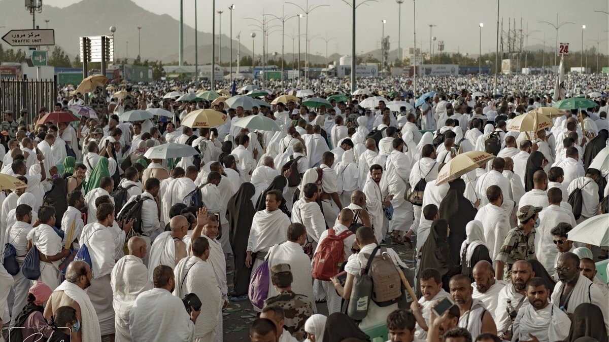 A large crowd of pilgrims in white Ihram sheets, many holding umbrellas against the sun