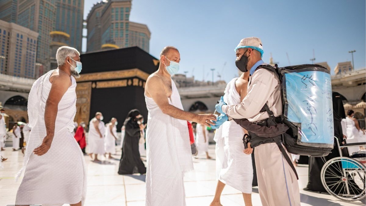 A worker offers hand sanitizer to pilgrims in Ihram in the courtyard of Masjid al-Haram