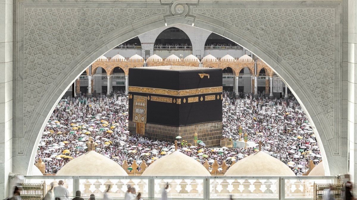 The Kaaba and a crowded mataf seen through an arch from an upper floor of Masjid al-Haram