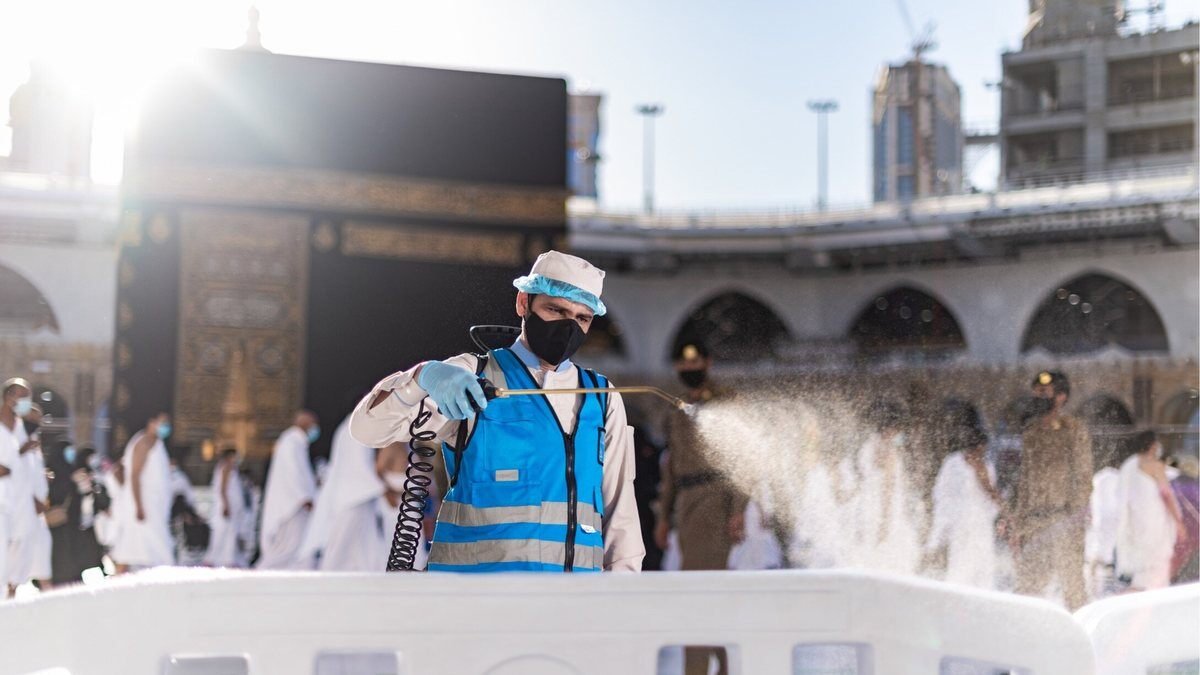 A worker in protective clothing spraying disinfectant on the marble near the Kaaba in the Mataf