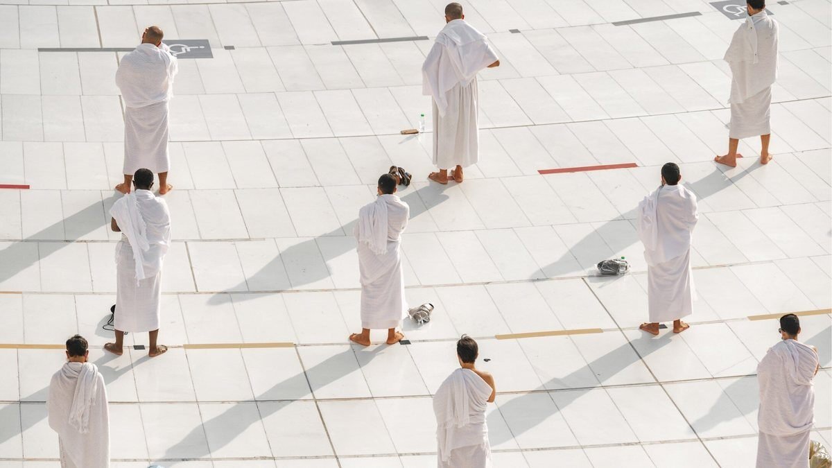 Men wearing two white Ihram sheets standing in the marble courtyard of Masjid al-Haram