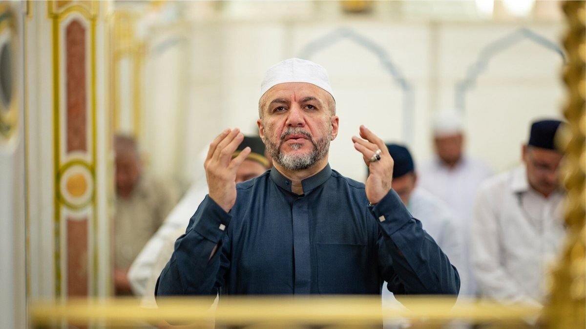 A pilgrim raising his hands in dua inside the mosque, with other worshippers behind him