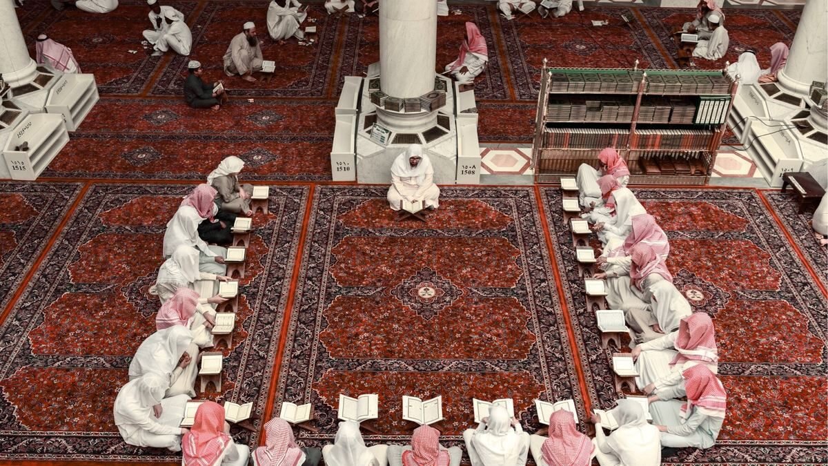 Pilgrims seated in a circle on the carpet of the Prophet's Mosque reading together after prayer