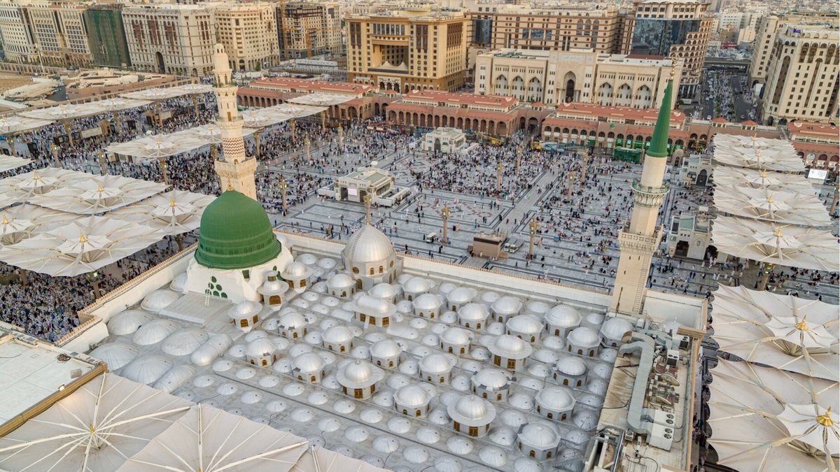 Aerial view of the Prophet's Mosque in Madinah with its courtyard umbrellas and the hotels of the central area