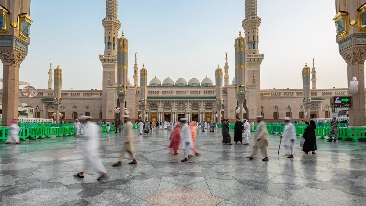 Pilgrims crossing the wide marble courtyard of the Prophet's Mosque in early morning light