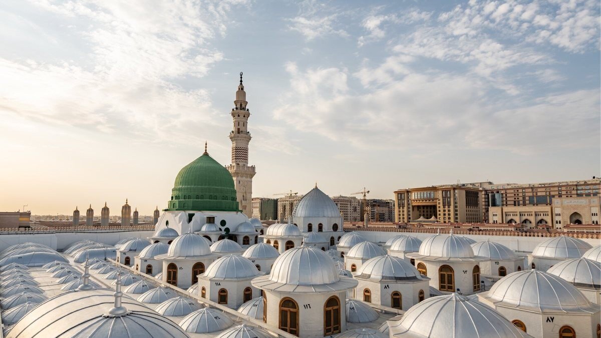 The Green Dome and a minaret of the Prophet's Mosque above rows of white courtyard umbrellas