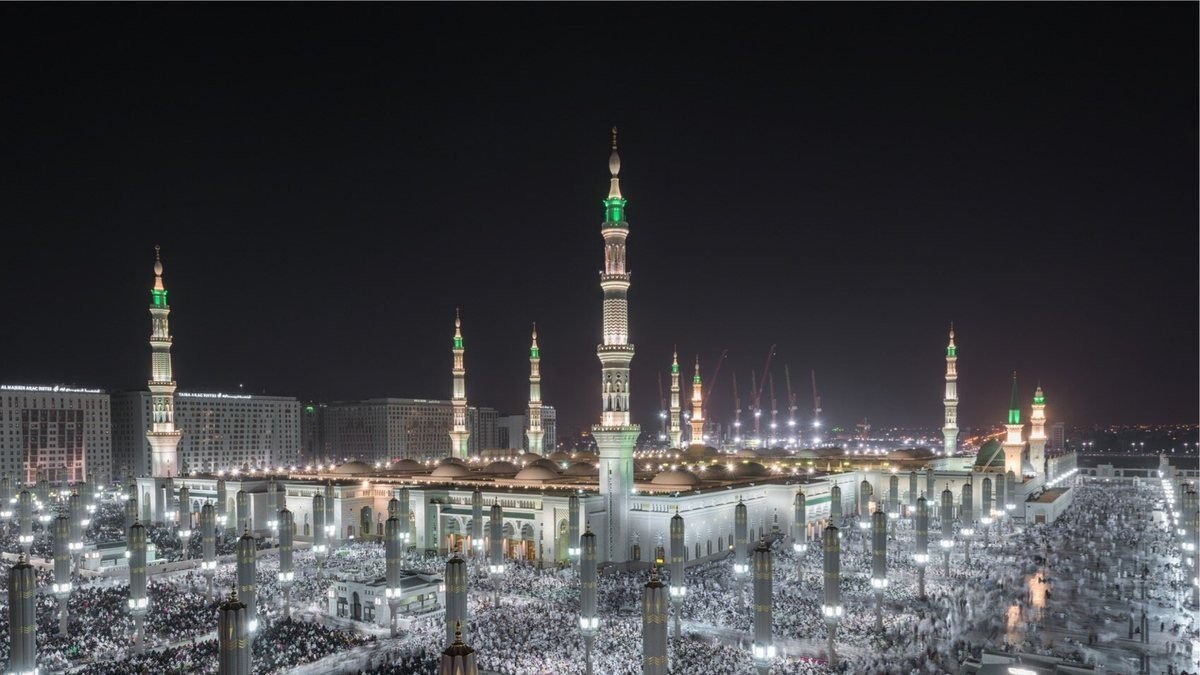 Worshippers filling the courtyards of the Prophet's Mosque in Madinah at night under its lit minarets