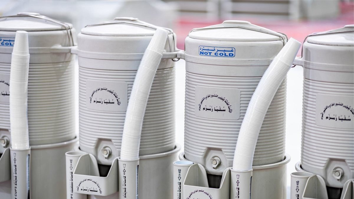 Row of white Zamzam water coolers with plastic cups and drinking taps